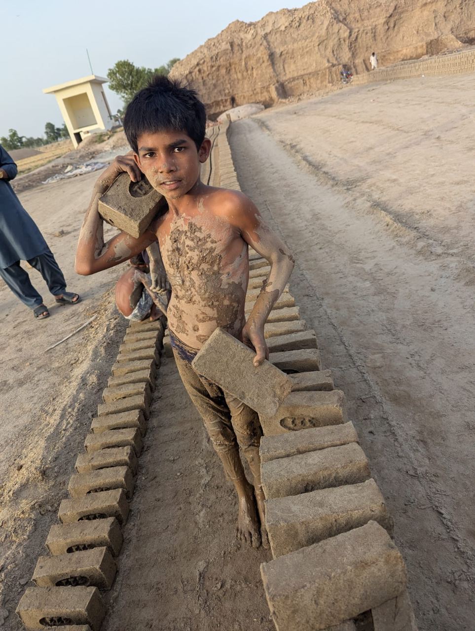 A boy carrying heavy bricks at a brick kiln