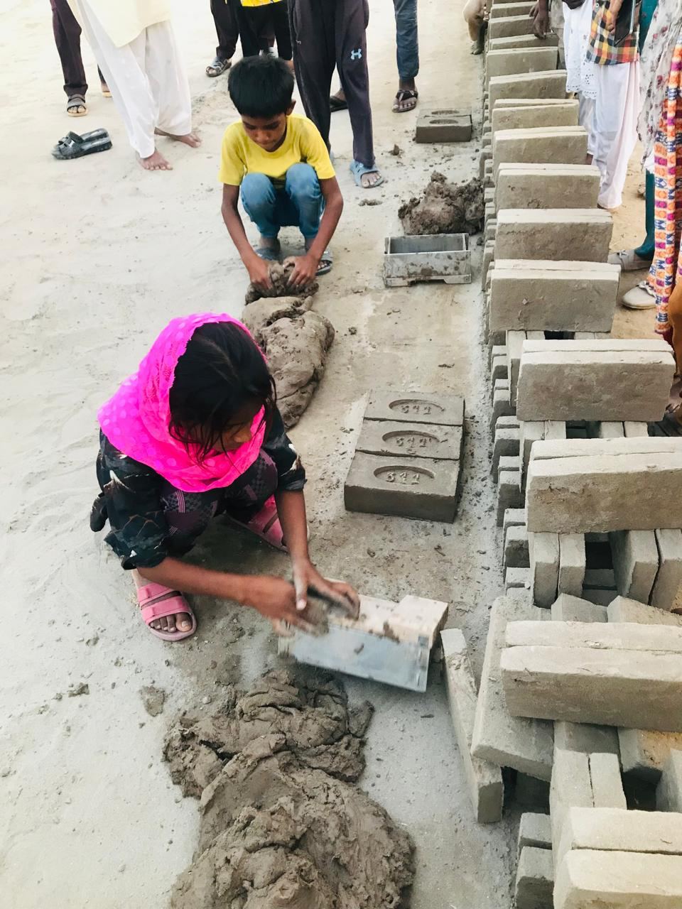 Two children molding bricks by hand at a brick kiln