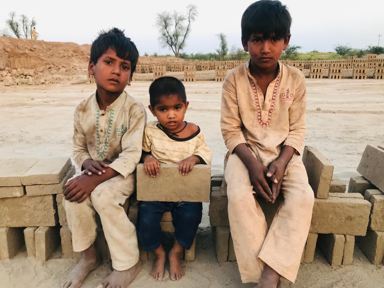 Three brothers sitting on bricks at a brick kiln